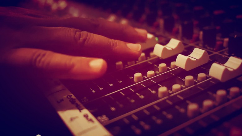 Close up of hands touching faders on a mixing console